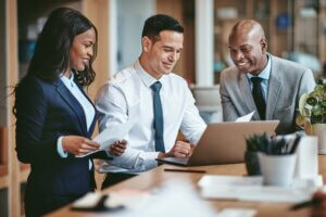 Smiling group of lawyers going over the law firm employee handbook together and working on a laptop at a table in an office
