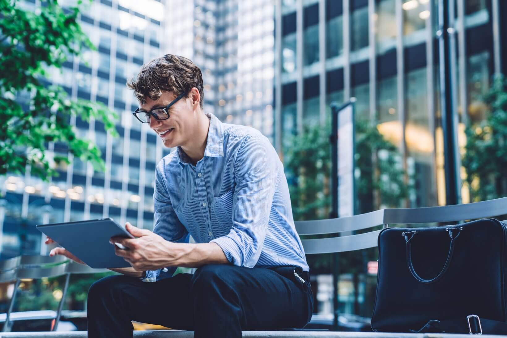 Cheerful young start-up attorney in formal wear looking at a tablet outside