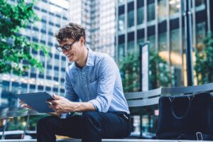 Cheerful young start-up attorney in formal wear looking at a tablet outside