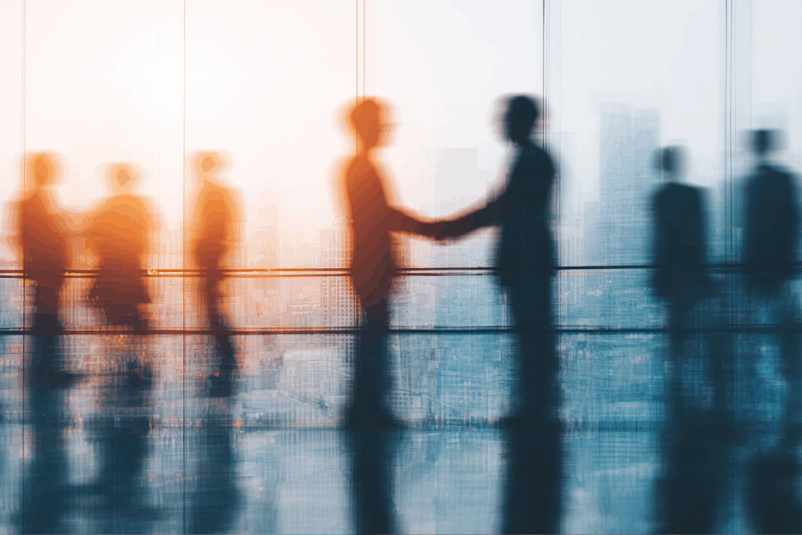 Silhouettes of two people shaking hands in a high-rise building with the sunset in the distance