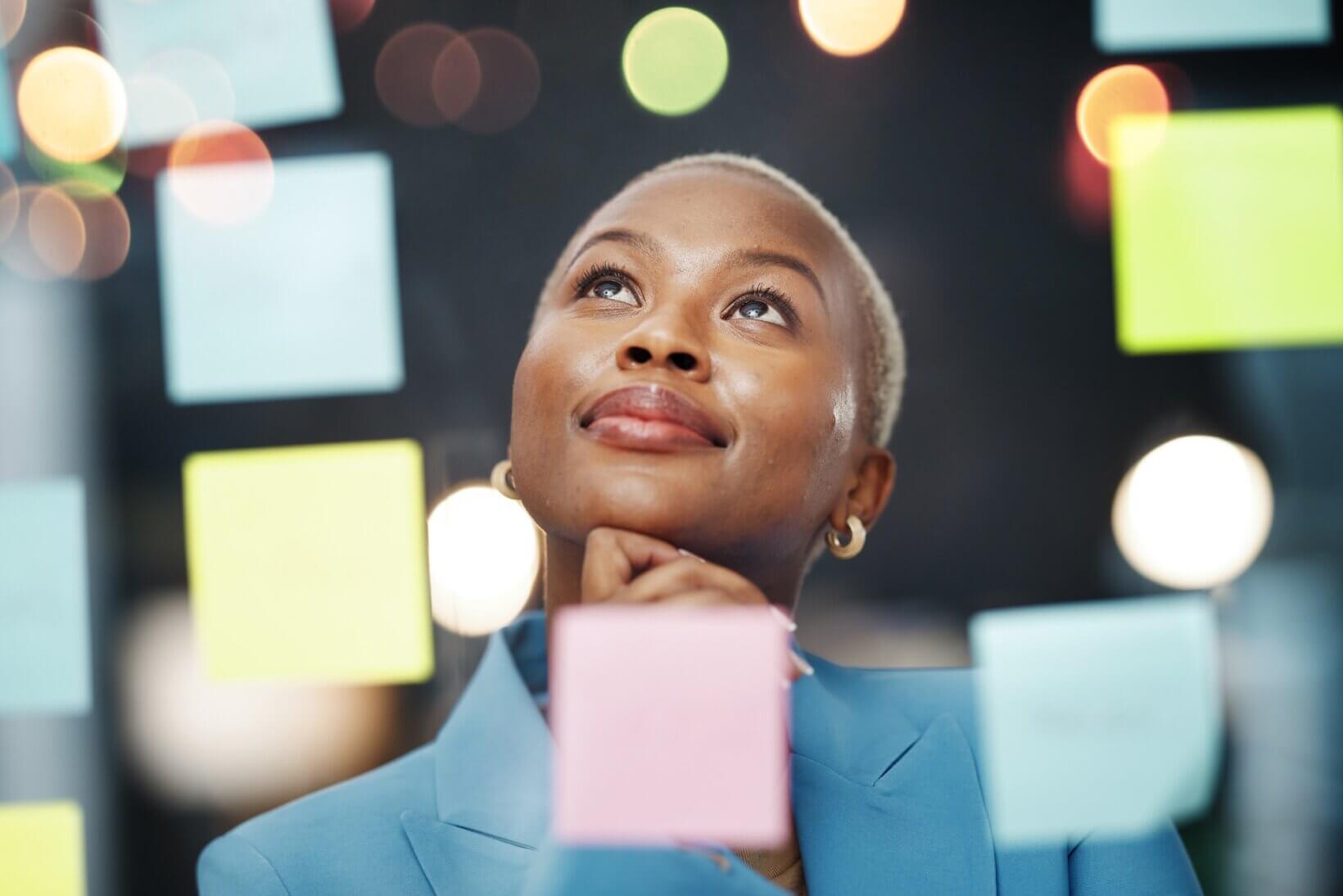 A woman looking at post it notes on a clear screen representing design thinking